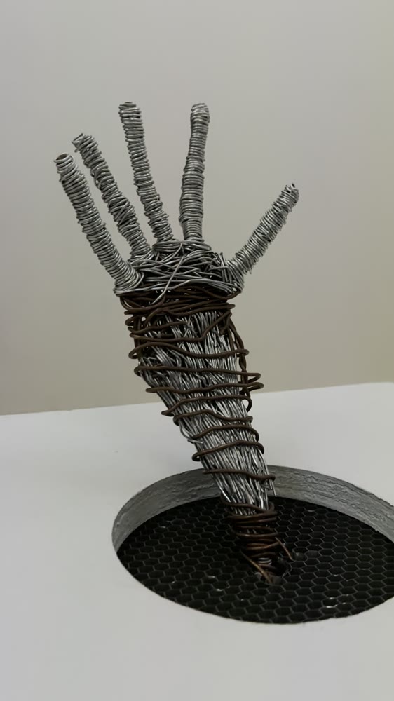 A wire sculpture of a hand reaching up out of a dark opening
